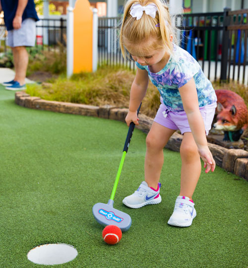 Child using small plastic golf club to hit a golf ball made of tennis ball material.